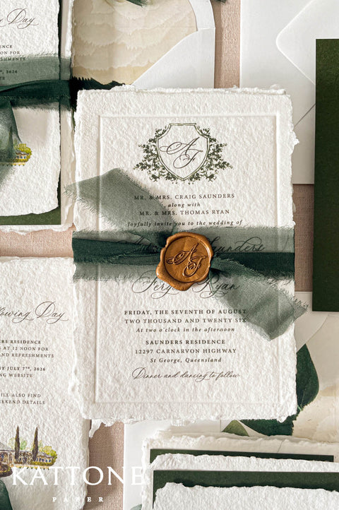 Wedding stationery arranged in a luxury flat lay showcasing handmade paper invitations, vellum wraps, green backing cards, ribbon, wax seals, and coordinated inserts.