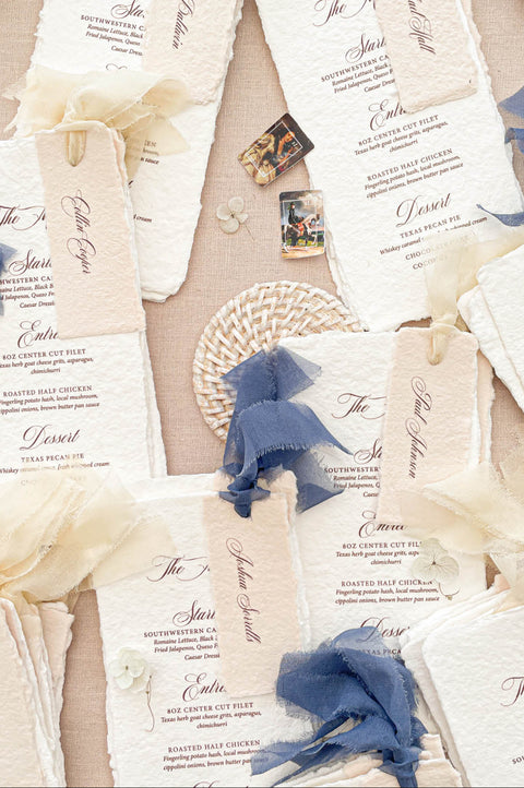 Luxury handmade paper wedding menus featuring deckled edge cotton paper, personalized guest name tags, elegant typography, and chiffon ribbon styling.