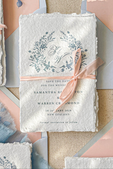 Announce your wedding with elegance and artistry through our handmade paper Save the Date cards, adorned with a soft blue watercolor floral wreath and tied with a delicate blush silk ribbon. Each card is crafted on luxury 100% cotton handmade paper with naturally torn deckled edges, creating a timeless and romantic keepsake that beautifully reflects your love story.