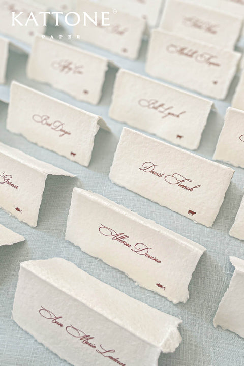 Elevate your table setting with our folded handmade paper place cards, crafted from luxurious deckled-edge cotton paper. Each card features elegant script printing and a petite icon detail, creating a timeless and refined look for weddings, events, and intimate gatherings. Their folded design allows them to stand beautifully on any tablescape, adding effortless sophistication.