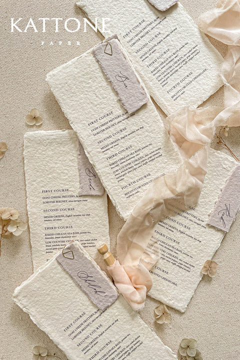 These handmade paper wedding menus embody the essence of soft romance and fine art elegance. Crafted from luxurious 100% cotton rag paper, each piece features delicate deckled edges and a naturally soft texture that enhances its artisanal appeal. The minimalist typography is printed in rich, elegant ink, paired with a vellum-inspired place card and silky blush ribbon, creating a layered and ethereal look perfect for modern romantic tablescapes.