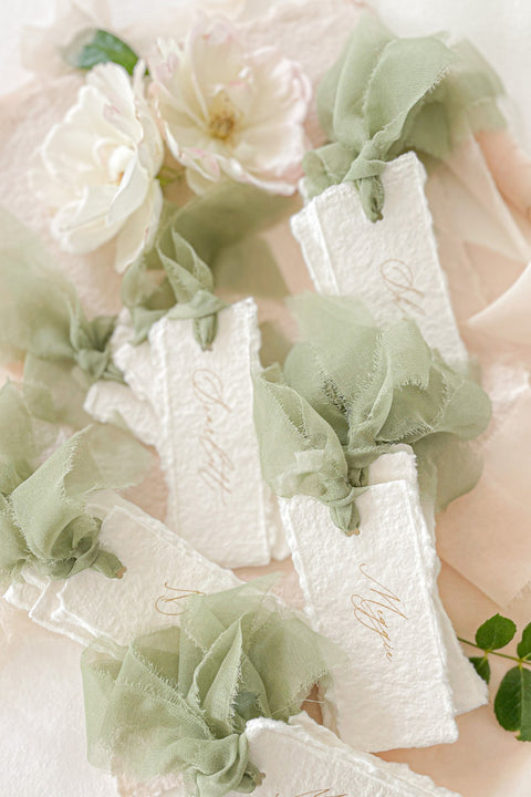 Bring soft, romantic elegance to your event with our handmade paper place cards, crafted from luxurious cotton rag paper and finished with natural deckled edges. Each card is adorned with airy sage-green chiffon ribbon and delicate calligraphy, creating a refined fine-art look perfect for weddings, showers, garden celebrations, and intimate gatherings. These artisanal place cards add movement, texture, and timeless beauty to any tablescape.