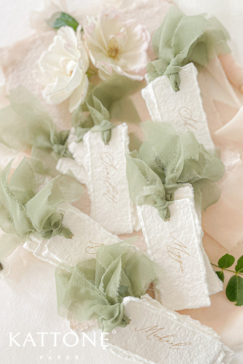 Bring soft, romantic elegance to your event with our handmade paper place cards, crafted from luxurious cotton rag paper and finished with natural deckled edges. Each card is adorned with airy sage-green chiffon ribbon and delicate calligraphy, creating a refined fine-art look perfect for weddings, showers, garden celebrations, and intimate gatherings. These artisanal place cards add movement, texture, and timeless beauty to any tablescape.
