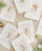 Handmade cotton paper paired with warm gold typography creates a refined and personalized table number design that elevates your seating presentation. Each card features a striking gold numeral centered above a beautifully arranged guest list, offering both elegance and functionality. The natural deckle edges and soft paper texture add an organic, fine-art feel - perfect for classic, luxurious, and romantic wedding aesthetics.