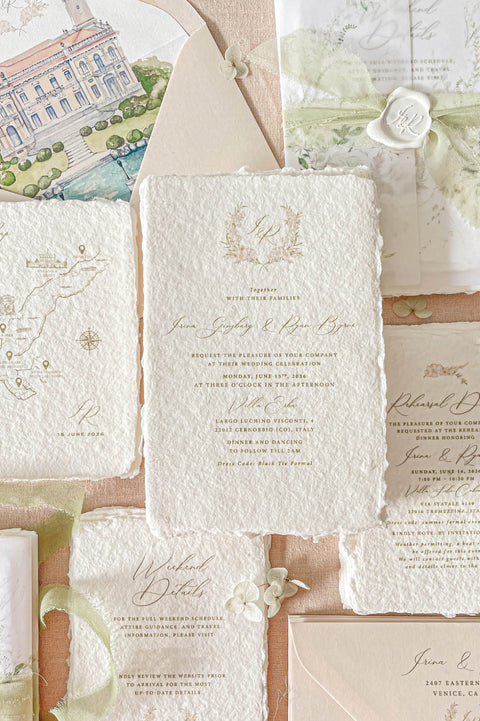 Luxury handmade paper wedding invitation suite featuring deckled edge cotton paper, custom watercolor venue artwork, vellum wraps, sage chiffon ribbon, personalized wax seals, and coordinating inserts in soft neutral tones.