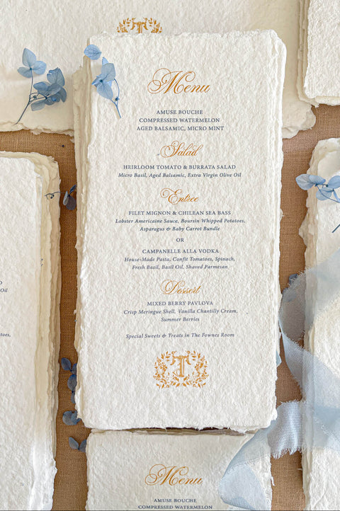 Luxury handmade paper wedding menus featuring deckled edge cotton paper, elegant gold script headings, blue typography, and delicate floral styling.