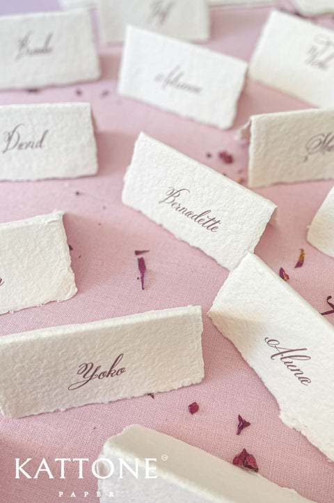 Handmade paper wedding place cards with deckled edges and calligraphy guest names, fine art table styling on blush linen.