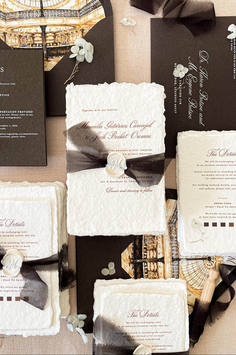 Luxury handmade paper wedding invitation suite featuring deckled edge cotton paper, custom architectural venue artwork, chocolate brown envelopes with illustrated liners, black chiffon ribbon wraps, and personalized wax seals.