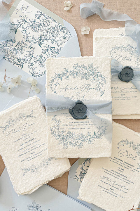Luxury handmade paper wedding invitation suite featuring deckled edge cotton paper, delicate blue floral illustrations, powder blue chiffon ribbon, wax seal accents, and coordinating blue wedding stationery.