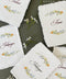 Watercolor floral handmade paper place cards featuring soft deckled edges, hand-torn cotton paper, and elegant calligraphy table names framed by delicate botanical florals in muted garden tones.