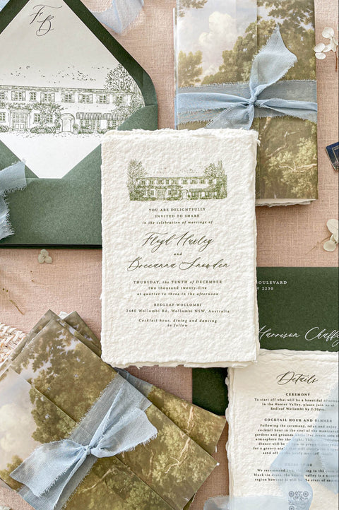 Luxury handmade paper wedding invitation suite featuring deckled edge cotton paper, custom venue sketch illustration, scenic vellum wraps, sage green envelopes, and powder blue chiffon ribbon styling.
