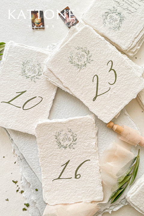 Watercolor greenery and handmade deckle-edge cotton paper create a naturally elegant table number design that brings soft, organic beauty to your wedding décor. The delicate botanical wreath and refined numeral style add a fine-art, timeless touch, making each card feel both romantic and elevated. Perfect for garden weddings, outdoor celebrations, and nature-inspired themes, this design blends airy watercolor tones with luxurious craftsmanship.