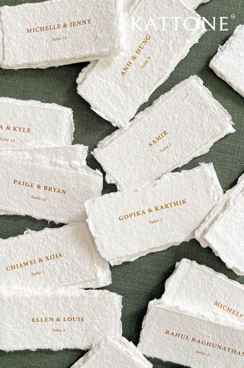 Handmade paper escort cards with deckled edges and gold guest names, luxury wedding seating cards on textured cotton paper.