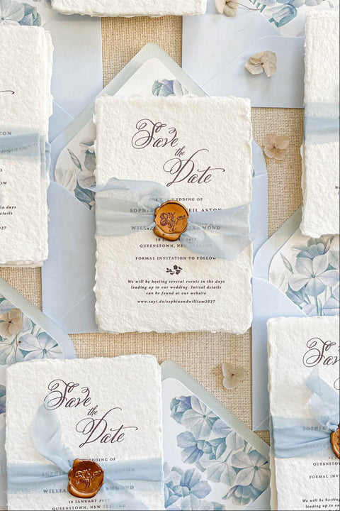 Announce your wedding with grace and artistry through our handmade paper Save the Date cards, featuring a blue hydrangea design, vellum wrap, and gold wax seal. Printed on luxury 100% cotton handmade paper with natural deckled edges, each card exudes elegance, texture, and timeless romance - perfect for fine art and destination weddings.