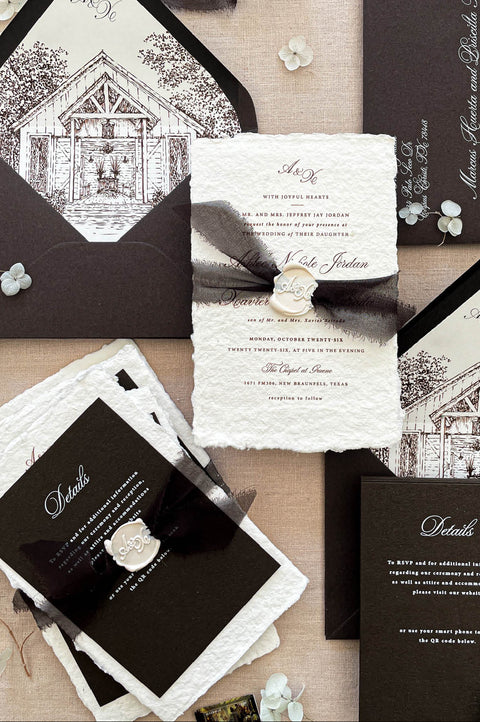 Luxury handmade paper wedding invitation suite with deep espresso envelopes, chapel illustration liners, black ribbon, and wax seal.