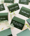 Folded green wedding place cards with white calligraphy, styled for a garden wedding reception.