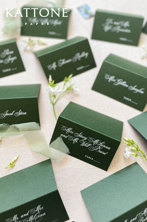 Folded green wedding place cards with white calligraphy, styled for a garden wedding reception.