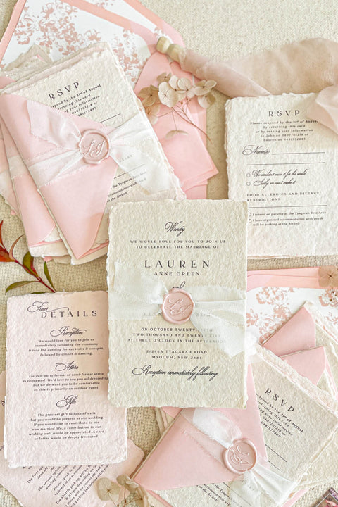 This handmade paper wedding invitation suite exudes timeless elegance with a touch of modern artistry. Crafted on luxury cotton paper with deckled edges, each invitation tells a story of care and craftsmanship. The delicate texture pairs beautifully with blush and ivory tones, creating a look that feels both classic and ethereal. Every detail is completed with a wax seal monogram, adding a touch of old-world refinement.