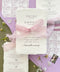 Luxury handmade cotton paper wedding invitation with deckled edges wrapped in blush silk ribbon, styled with lavender envelopes and botanical envelope liners.
