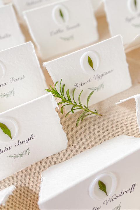 Add an organic, fine-art touch to your event with our handmade paper place cards, crafted from luxurious cotton rag paper with naturally torn deckled edges. Each card features a white botanical wax seal embedded with a real leaf, paired with elegant calligraphy for a soft, romantic aesthetic. Perfect for weddings, garden celebrations, and refined gatherings, these artisan-crafted place cards bring natural beauty and timeless charm to any tablescape.