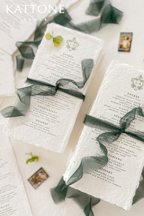 Elevate your reception table styling with our handmade paper wedding menus, printed on luxurious 100% cotton paper with soft deckled edges and adorned with an elegant crest monogram. Each menu captures the timeless charm of fine-art stationery, blending artisanal craftsmanship with modern sophistication. Finished with a hand-tied deep green silk ribbon.