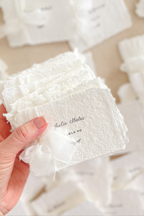 Elevate your event with our handmade paper place cards, crafted from luxurious cotton rag paper and finished with soft, natural deckled edges. Each card is delicately wrapped with fine chiffon ribbon and printed in elegant calligraphy, creating a timeless, romantic detail for weddings, bridal showers, and upscale celebrations. These artisan-crafted pieces add a soft, ethereal charm to any tablescape and photograph beautifully for your flatlays.