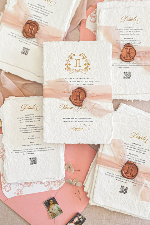 Handmade paper wedding invitations with custom monogram crest, blush silk ribbon, wax seal detail, and deckle edge cotton paper.