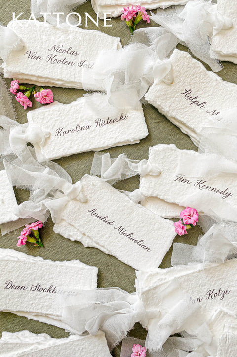 Handmade paper wedding place cards with deckled edges and soft silk ribbon, fine art table styling with blush florals.