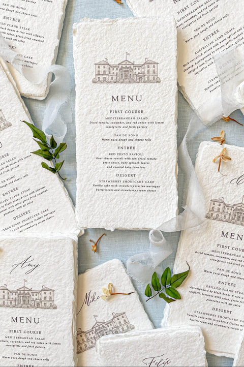 Handmade paper wedding menu with deckled edges and custom venue illustration, fine art reception stationery flat lay.