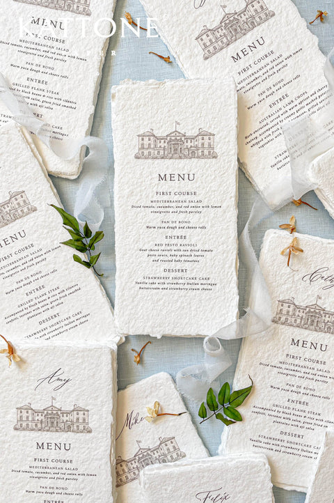 Handmade paper wedding menu with deckled edges and custom venue illustration, fine art reception stationery flat lay.