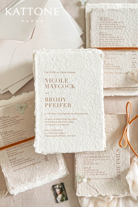 Luxury handmade cotton paper wedding invitation with deckled edges and warm terracotta typography, styled with neutral envelopes, ribbon accents and coordinated stationery suite on soft beige background.
