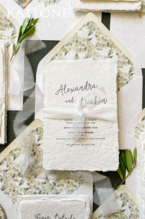 Handmade paper wedding invitation with deckled edges, soft calligraphy typography, ivory silk ribbon, romantic fine art wedding stationery flat lay.
