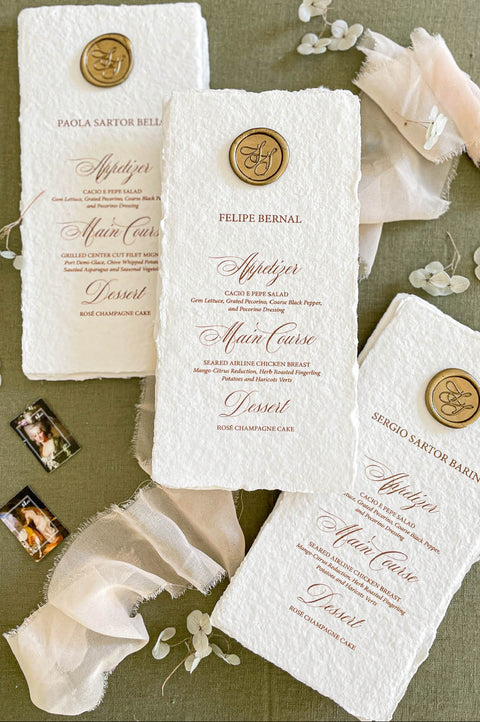 Handmade cotton paper wedding menus with deckled edges and elegant calligraphy typography, styled with wax seal accents and soft chiffon fabric.