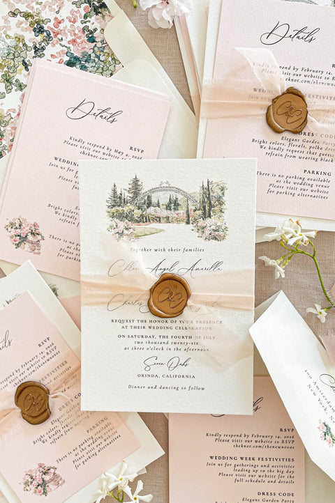Wedding invitations with a custom watercolor venue illustration, printed on textured handmade paper with silk ribbon and wax seal details.