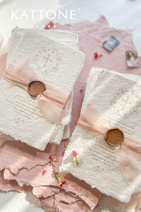 A soft and faith-inspired christening invitation handcrafted from luxurious cotton rag paper and finished with blush silk ribbon and a classic wax seal. Featuring a delicate watercolor floral wreath and Christian cross, this design blends tenderness, tradition, and fine-art elegance. Perfect for baptisms and christenings, it creates a heartfelt keepsake to celebrate this sacred milestone.