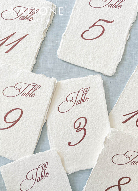 These handmade cotton paper table numbers feature elegant burgundy script printed on richly textured deckle-edge sheets for a timeless fine-art look. The warm, sophisticated lettering paired with artisanal paper adds depth, character, and romance to any wedding tablescape. Ideal for classic, rustic-elegant, and modern romantic themes, this design brings effortless refinement to your reception layout.