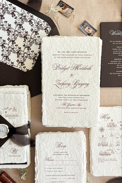Top-down flat lay of luxury brown wedding invitation suite featuring ivory handmade deckled-edge paper, chocolate brown envelopes, floral patterned envelope liner, custom wedding map card, RSVP card, dark details card, sheer dark ribbon, and personalized white wax seal
