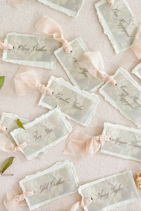 Add ethereal elegance to your event with our handmade paper place cards, crafted from delicate cotton rag paper and layered with a translucent vellum top sheet. Each card is finished with naturally torn deckled edges and soft blush ribbon, creating a dreamy fine-art look perfect for weddings, showers, and romantic celebrations. These unique layered cards bring texture, movement, and refined beauty to every tablescape.