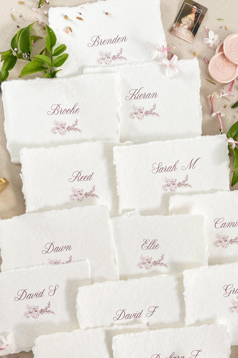 Bring soft elegance to your tablescape with our handmade paper place cards, crafted from luxurious cotton rag paper and finished with naturally torn deckled edges. Each card features romantic calligraphy paired with a delicate floral illustration, creating a fine-art aesthetic perfect for weddings, showers, intimate dinners, and elevated celebrations. These artisan-crafted pieces add organic texture, timeless beauty, and refined charm to any event setting.