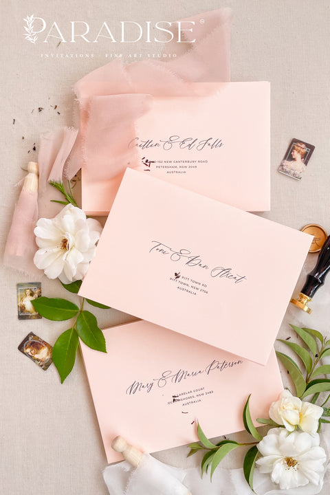 Elegant soft peach envelopes arranged with floral details and silk ribbon for fine art wedding invitations.