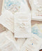 Luxury handmade cotton paper wedding invitation with deckled edges and gold typography, styled with wax seal, vellum wrap and watercolor Greek church envelope liners.