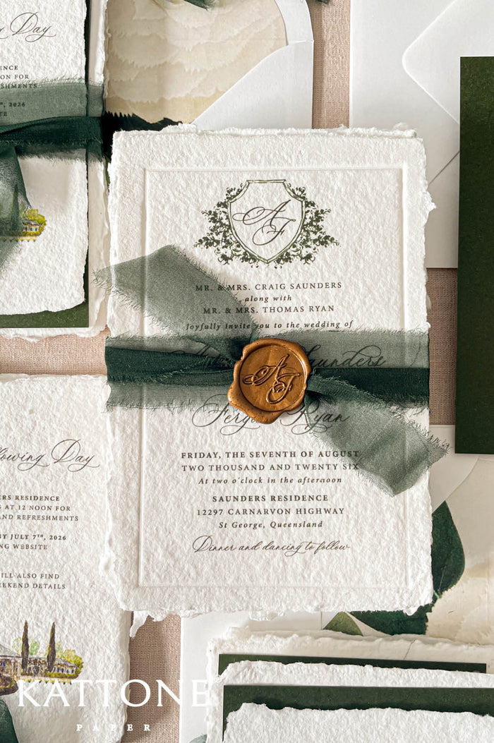 Wedding stationery arranged in a luxury flat lay showcasing handmade paper invitations, vellum wraps, green backing cards, ribbon, wax seals, and coordinated inserts.