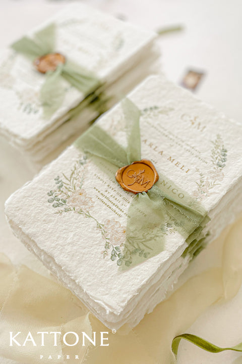 These handmade paper engagement invitations are a true keepsake for life’s most meaningful moments. Printed on luxury deckled-edge cotton paper, each piece showcases the soft texture and organic edges that make handmade paper so timeless and special. Adorned with watercolor botanical illustrations in gentle sage and blush tones, the design radiates natural elegance. The suite is finished with a translucent green silk ribbon and wax seal featuring the couple’s monogram.