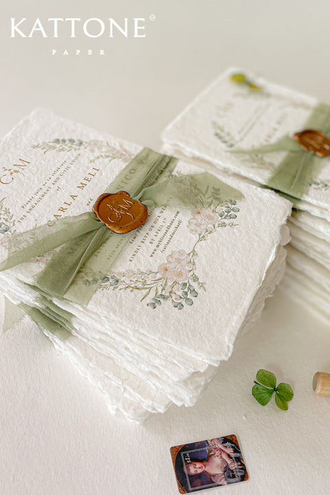 These handmade paper engagement invitations are a true keepsake for life’s most meaningful moments. Printed on luxury deckled-edge cotton paper, each piece showcases the soft texture and organic edges that make handmade paper so timeless and special. Adorned with watercolor botanical illustrations in gentle sage and blush tones, the design radiates natural elegance. The suite is finished with a translucent green silk ribbon and wax seal featuring the couple’s monogram.