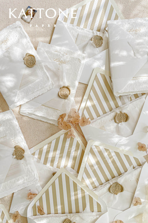 White wedding envelopes with envelope liners styled with silk ribbon, wax seals, and fine art stationery details on a neutral linen background.