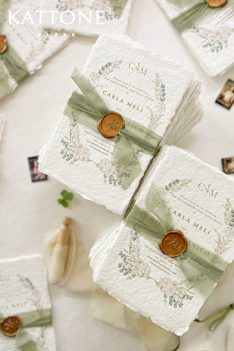 These handmade paper engagement invitations are a true keepsake for life’s most meaningful moments. Printed on luxury deckled-edge cotton paper, each piece showcases the soft texture and organic edges that make handmade paper so timeless and special. Adorned with watercolor botanical illustrations in gentle sage and blush tones, the design radiates natural elegance. The suite is finished with a translucent green silk ribbon and wax seal featuring the couple’s monogram.