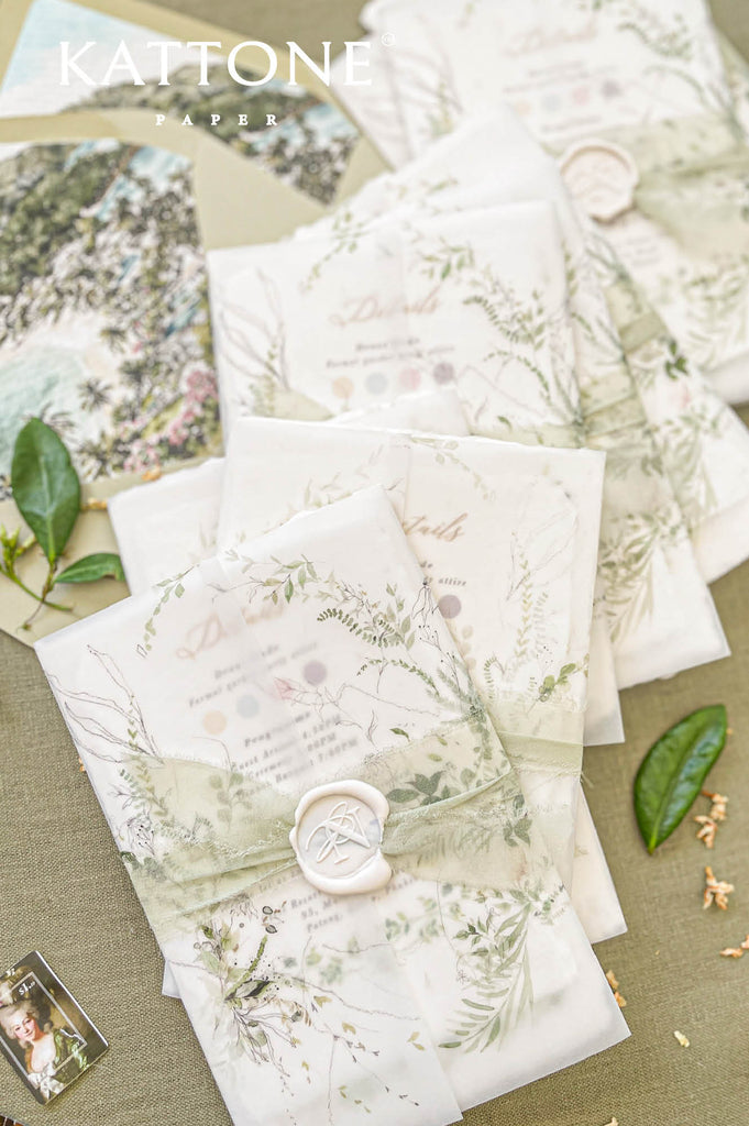 Wedding invitation wrapped in translucent vellum revealing botanical watercolor artwork on handmade paper.