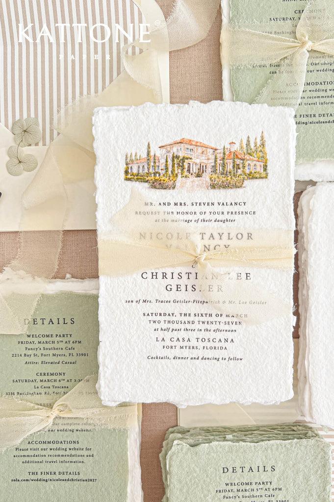 Detailed overhead photograph of a luxury deckled-edge wedding invitation featuring a hand-painted Tuscan-inspired villa with terracotta rooftops and cypress trees, elegant typography and sheer ivory ribbon, surrounded by sage green handmade paper details cards, an RSVP card and striped envelope liner.