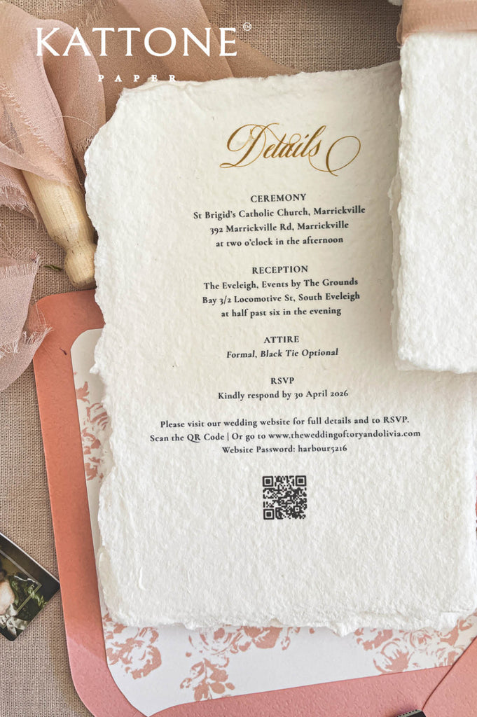 Close-up of handmade cotton paper wedding invitation featuring a gold monogram crest, textured deckle edges, and refined typography.