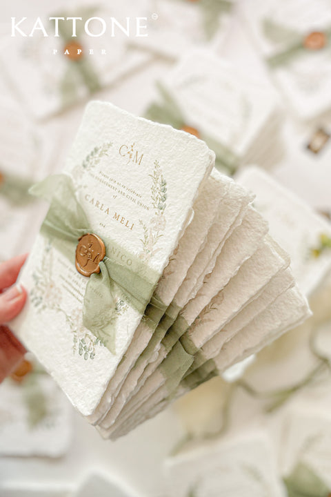These handmade paper engagement invitations are a true keepsake for life’s most meaningful moments. Printed on luxury deckled-edge cotton paper, each piece showcases the soft texture and organic edges that make handmade paper so timeless and special. Adorned with watercolor botanical illustrations in gentle sage and blush tones, the design radiates natural elegance. The suite is finished with a translucent green silk ribbon and wax seal featuring the couple’s monogram.